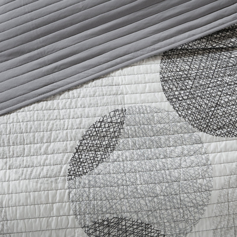 Graues Steppdecken-Set mit geometrischem Kreismuster auf einem Bett