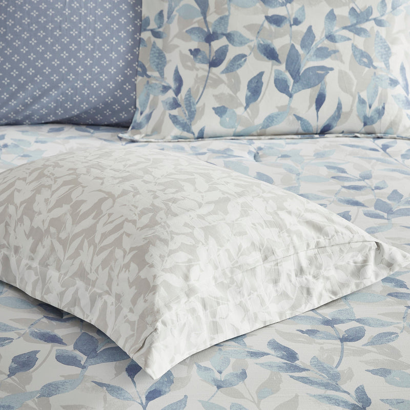 Blaues 8-teiliges Bettwäsche-Set mit wendbarer Bettdecke und Blättermuster auf einem Bett