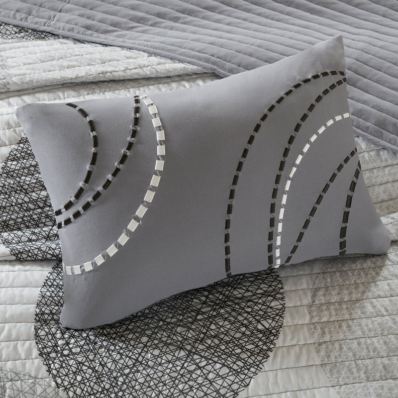 Graues Steppdecken-Set mit geometrischem Kreismuster auf einem Bett